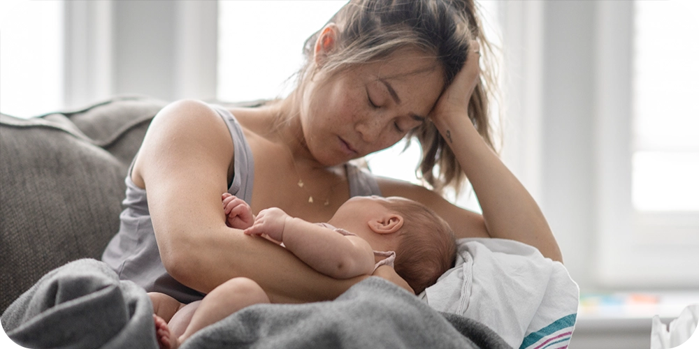 Tired and stressed mother holding her newborn while resting on her couch