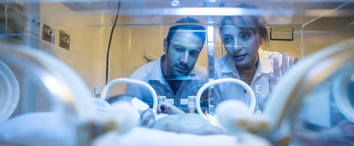 Parents of a premature infant gaze into an incubator